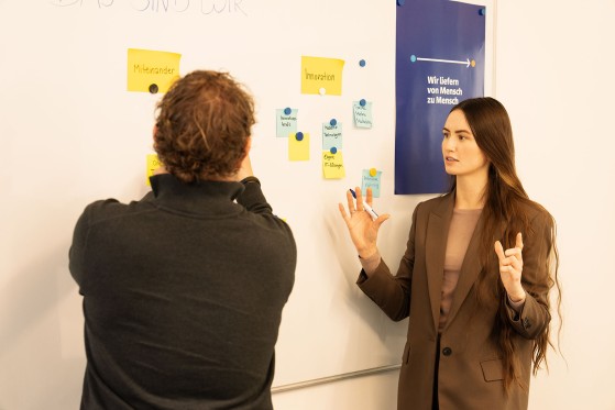 two employees are standing in front of the whiteboard and discussing