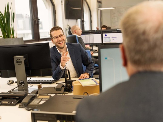 IT Employee in the open office space smiles at his colleague across from him