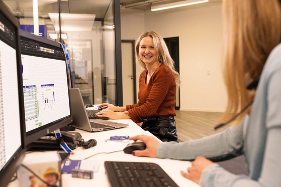 Employees working at the desk and one is smiling at her colleague 
