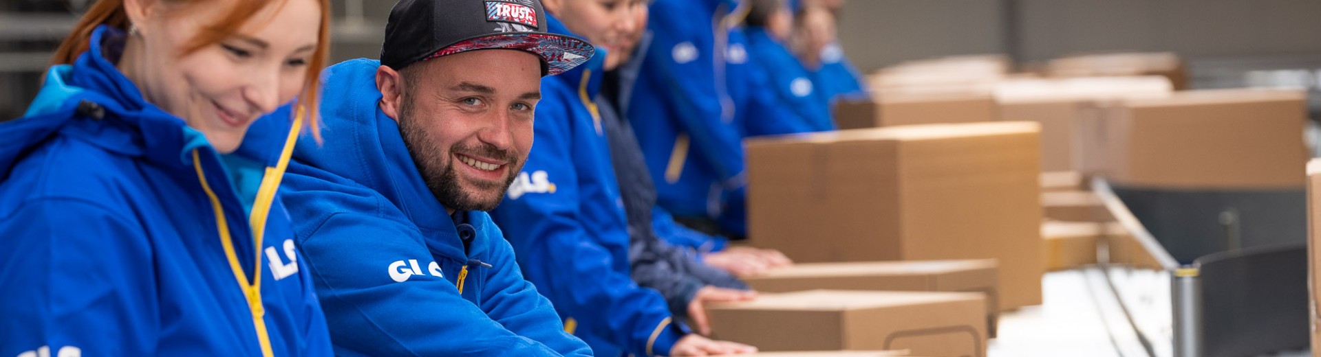 Employees are sorting packages on the conveyor belt one of them is smilling at the camera