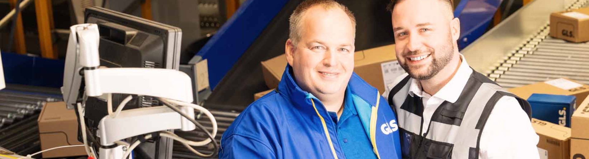 Managers standing in the depot in front of a conveyor belt and smiling into the camera