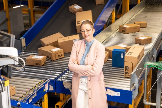 Young executive in the depot in front of a conveyor belt with packages smiles into the camera