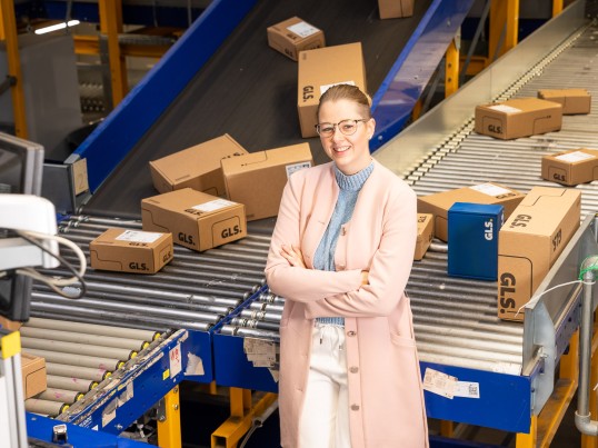 Young executive in the depot in front of a conveyor belt with packages smiles into the camera