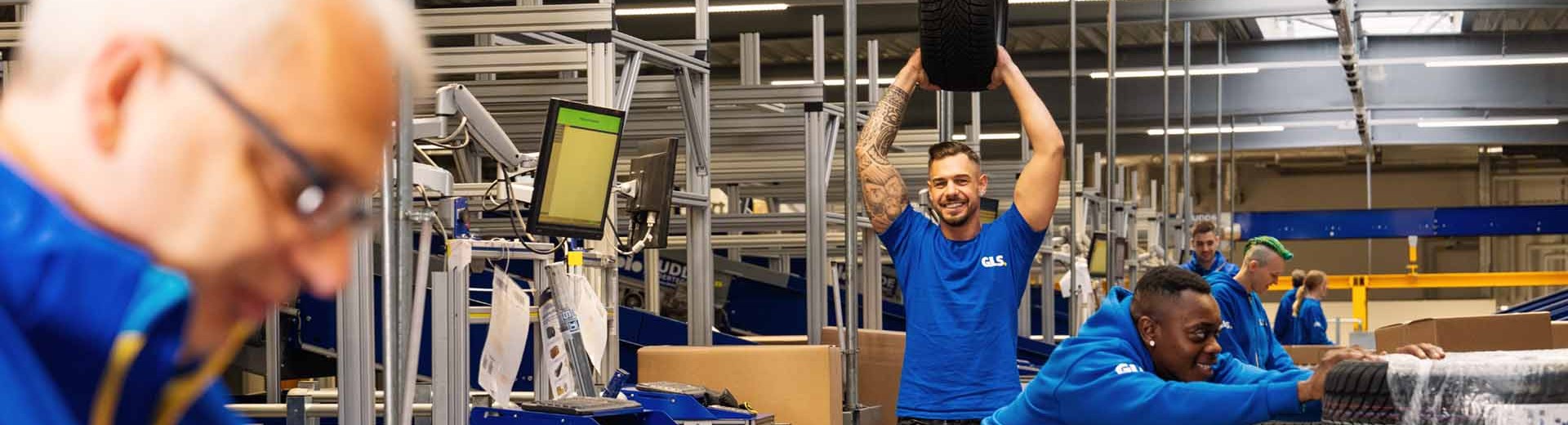Mitarbeitende arbeiten zusammen in der Halle, ein Kollege hält einen Autoreifen hoch