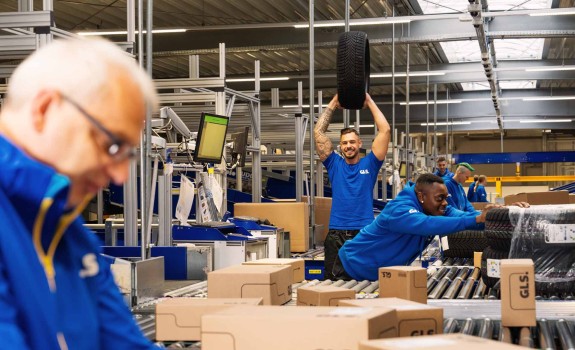 Mitarbeitende arbeiten zusammen in der Halle, ein Kollege hält einen Autoreifen hoch