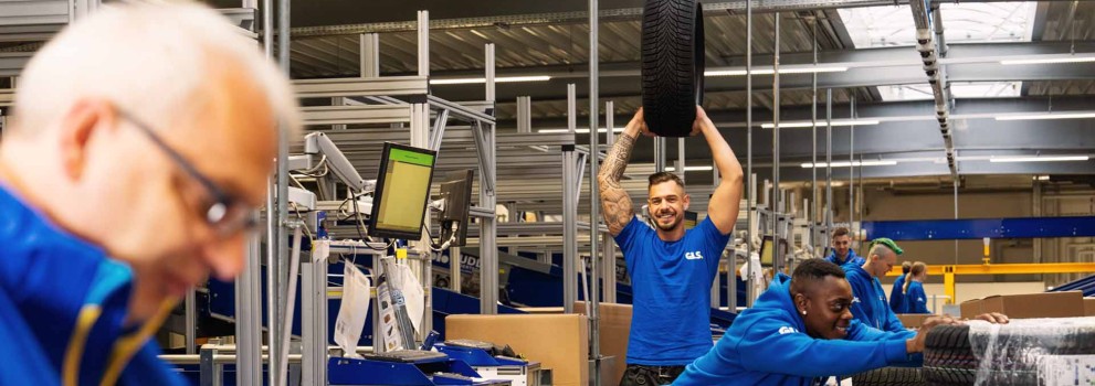 Mitarbeitende arbeiten zusammen in der Halle, ein Kollege hält einen Autoreifen hoch