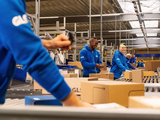 Mitarbeitende arbeiten gemeinsam in der Halle und legen Pakete auf die Bandanlage